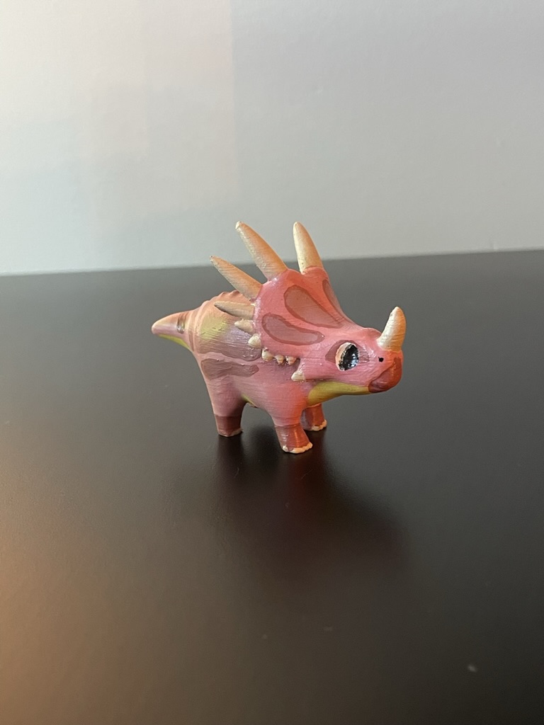 A 3D printed triceratops that has been painted pinks and yellows