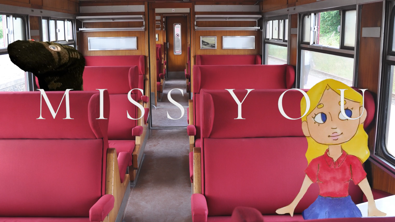 screenshot of video with a papercut doll and sock puppet dog riding a train. The text on the slide says "Miss You"