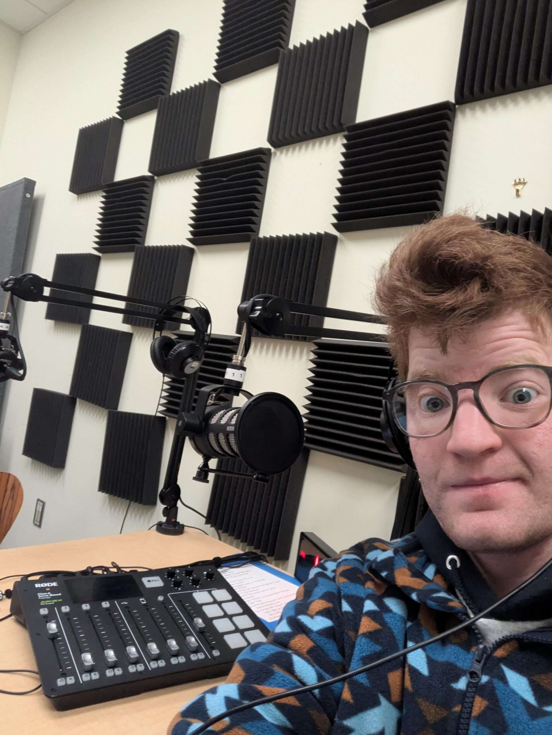 a wide-eyed young man in a podcast studio sitting in front of a mixer and microphone